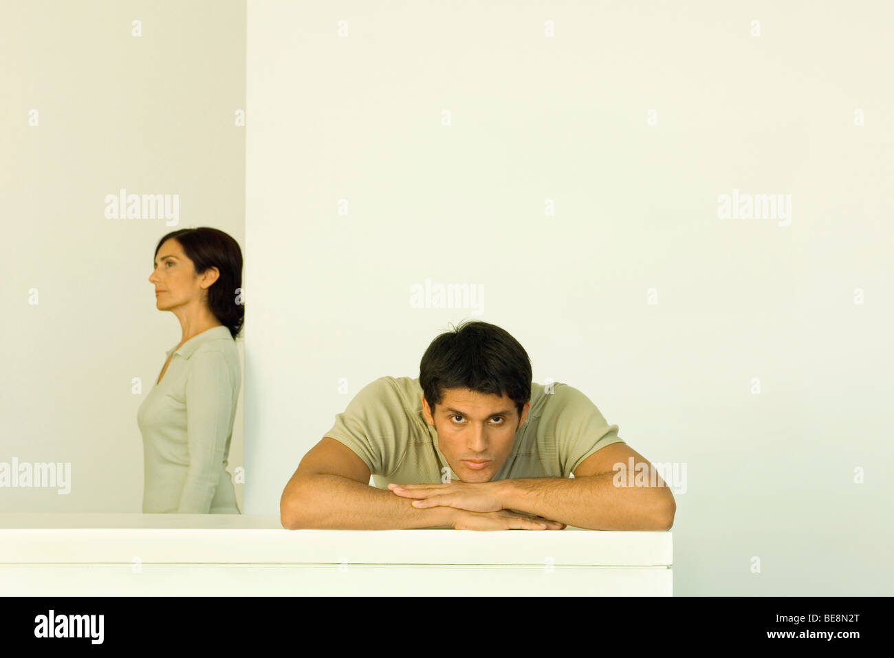 Man resting head on arms looking at camera, woman in background looking away Stock Photo
