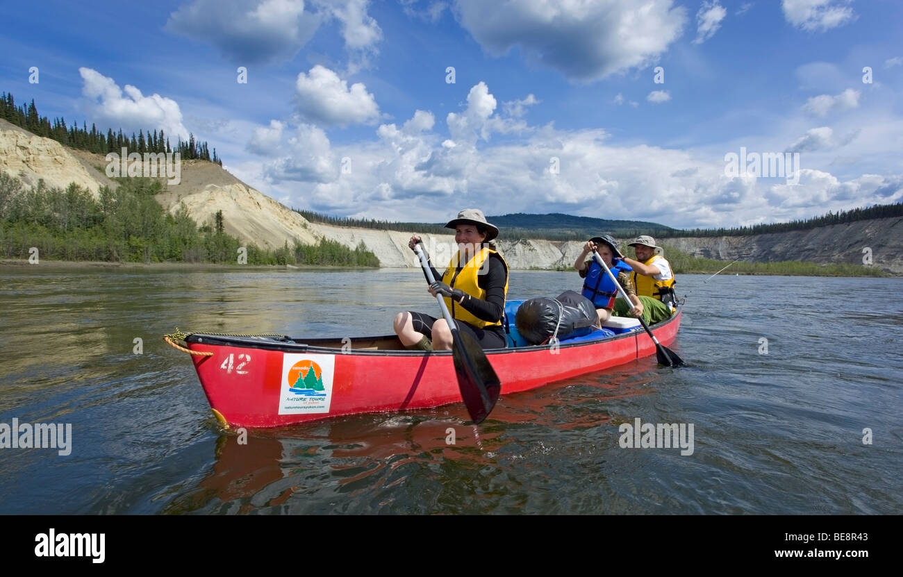 Family with young boy in a canoe, paddling, canoing on Teslin River, high cut bank behind, Yukon Territory, Canada Stock Photo