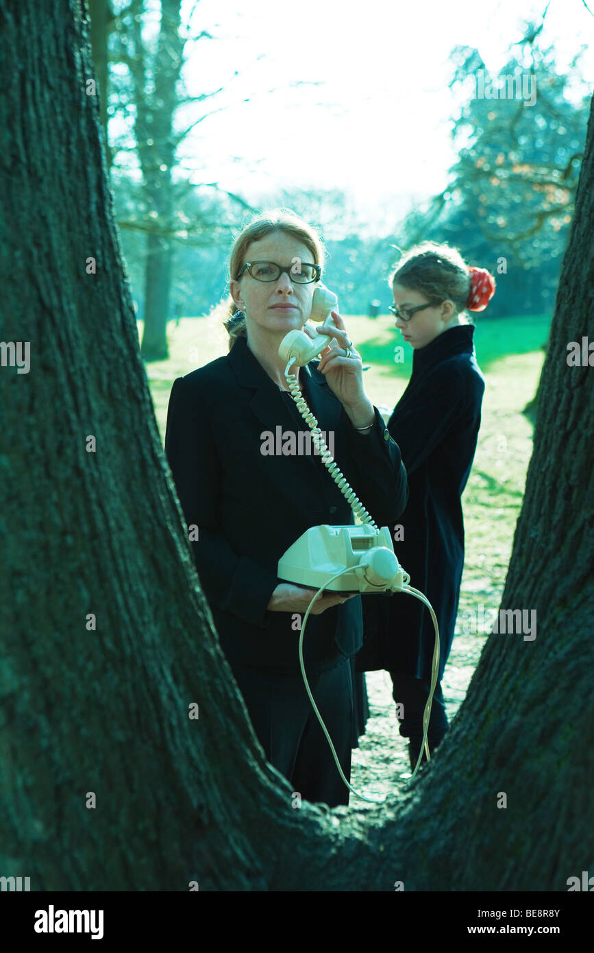 Woman standing beside tree trunk, using landline phone Stock Photo
