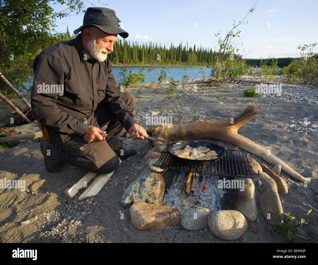 Man cooking, frying fish fillets in a pan on a camp fire, upper Liard River, Yukon Territory, Canada Stock Photo