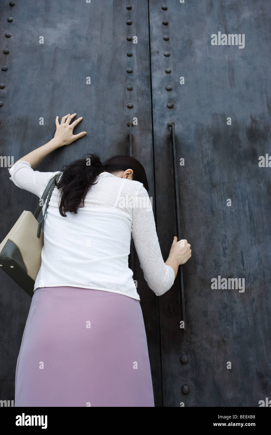 Woman standing beside closed door with head down, hand on door Stock Photo