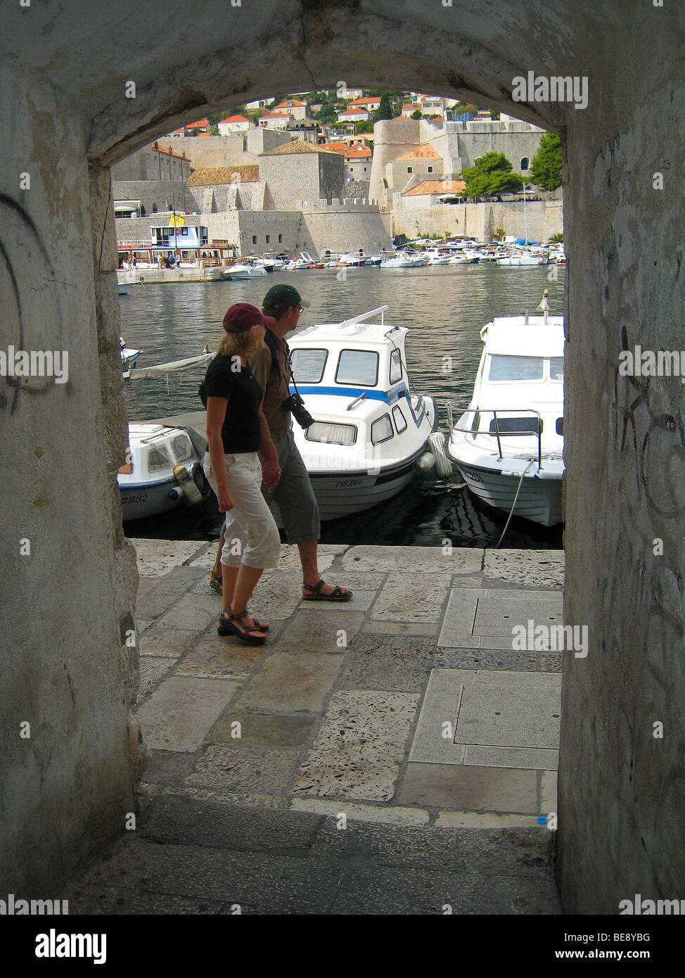Croatia; Hrvartska; Kroatien; Dubrovnik, Fishboat and small tourist boat harbor, harbour, couple walks by arch in wall. Stock Photo