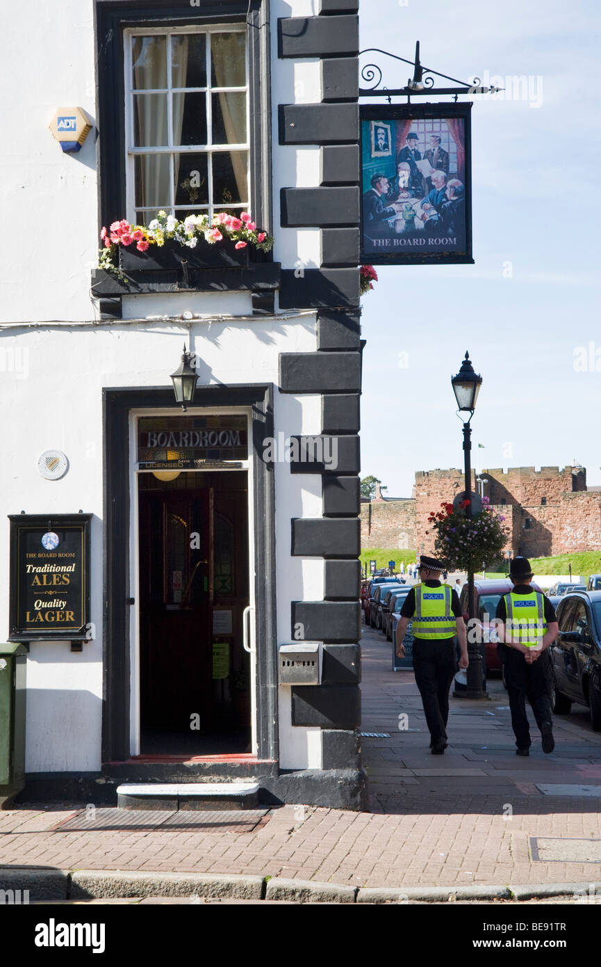 Two policemen walking past The Boardroom a public house in Carlisle, Cumbria, with Carlisle Castle in background, England, UK Stock Photo