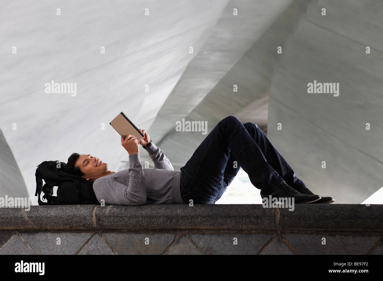 man lying down laying at back pack, reading a book Stock Photo