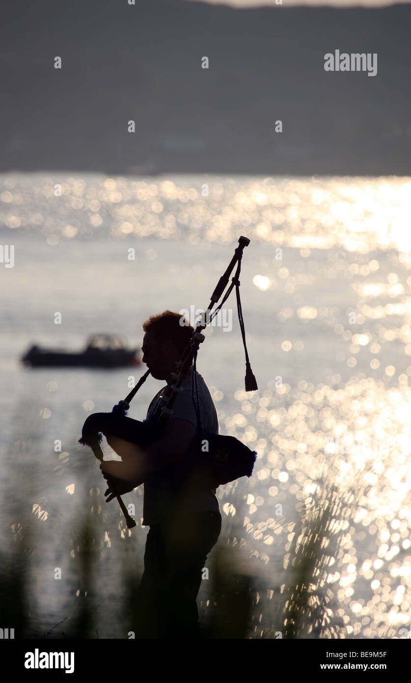 Piper playing the bagpipes against a shimmering Sound of Iona Stock
