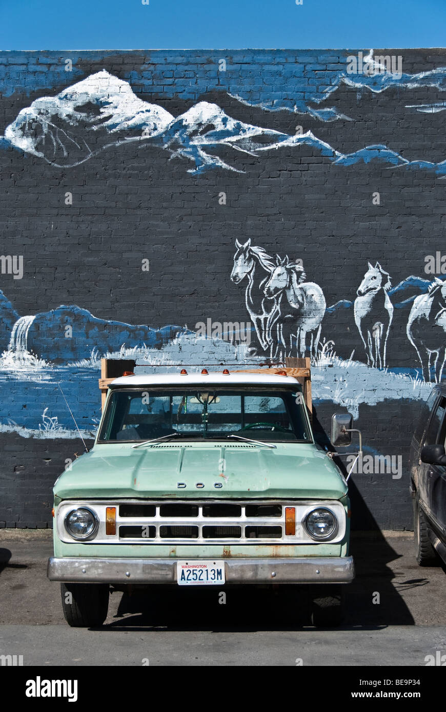 old late sixties Dodge truck parked in front of mural painted on brick wall depicting wild horses running in foothill country Stock Photo
