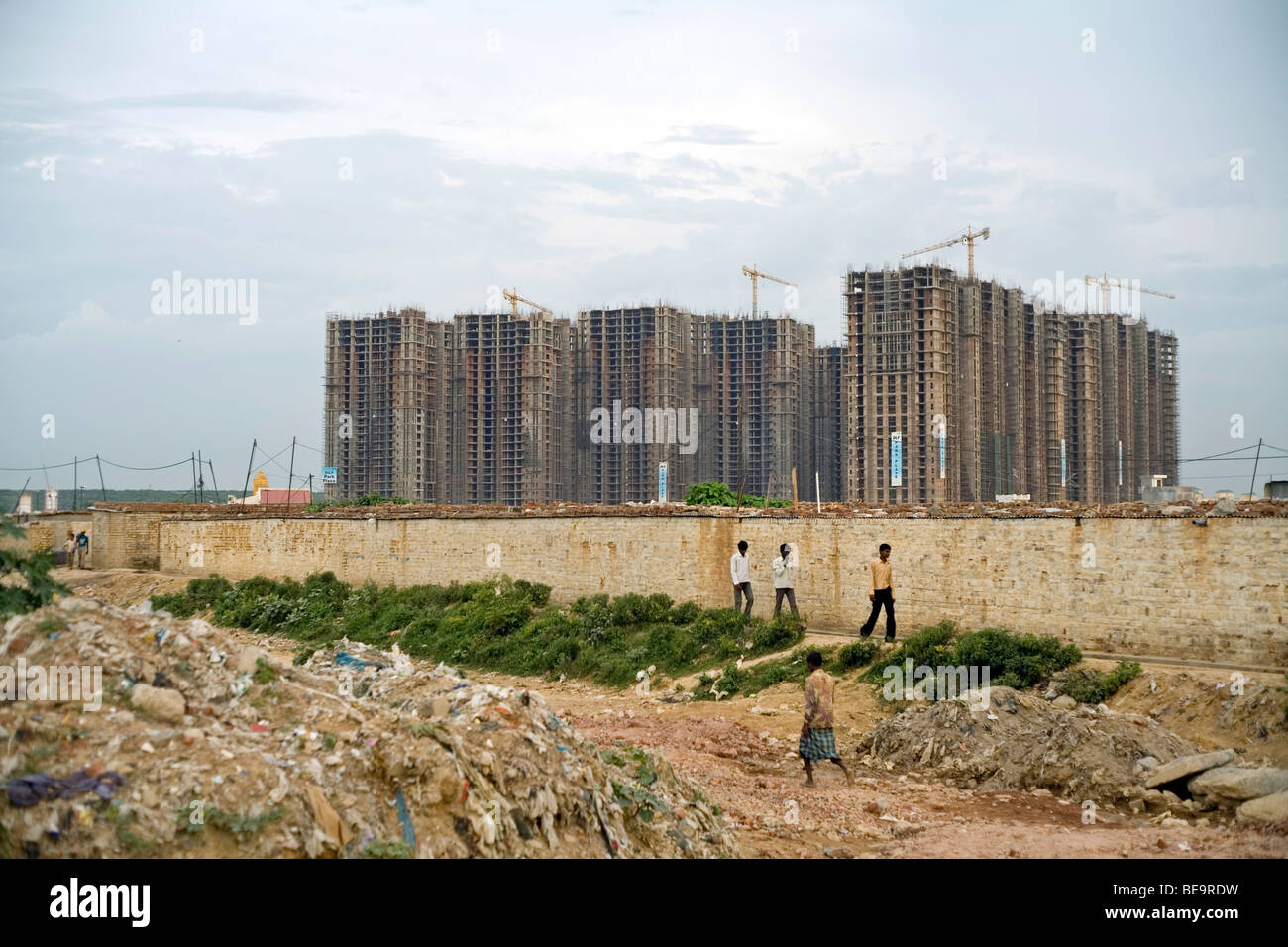 Men walking through a labour camp in the shadow of a new development in Gurgaon, India Stock Photo