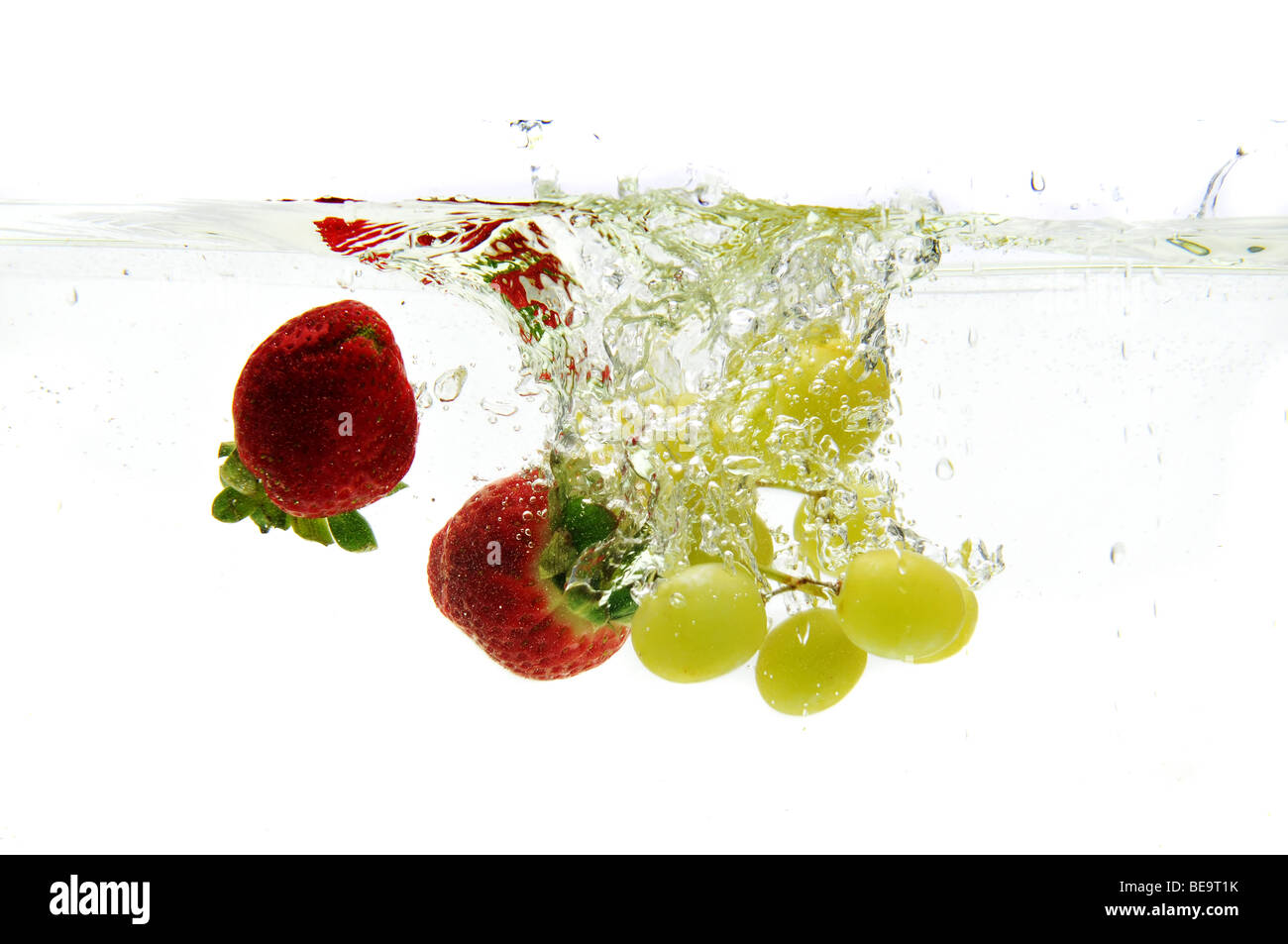 Strawberries and grapes dropped in the water isolated against a white background Stock Photo
