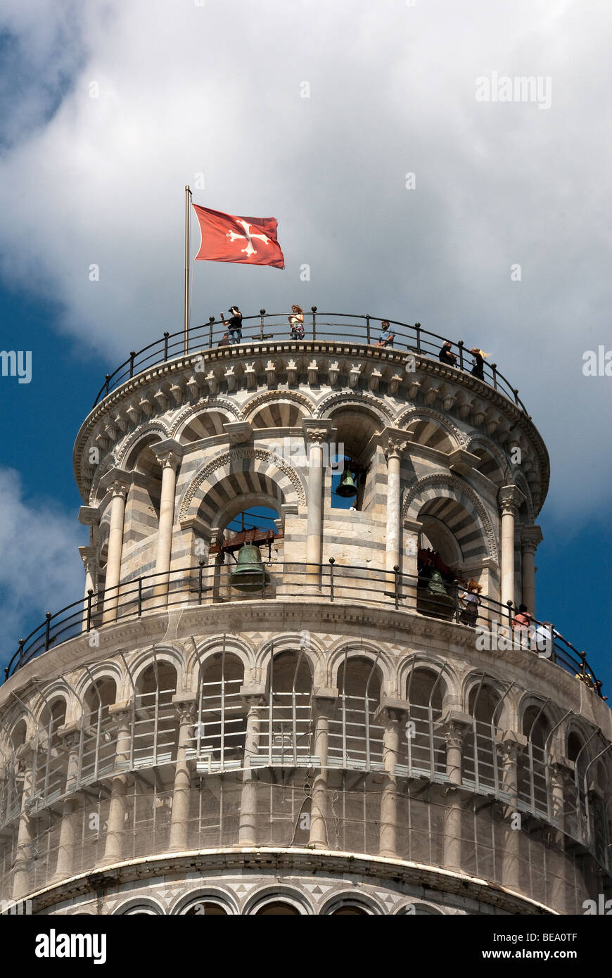 Tourists on top of the Leaning Tower of Pisa with red flag of Pisa with white Maltese Cross and sculpture of Cherubs Stock Photo