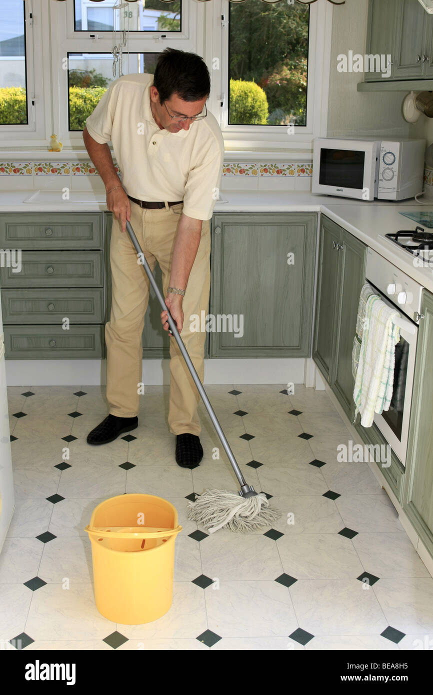 A Man Using A Mop And Bucket To Clean A Kitchen Floor Stock Photo
