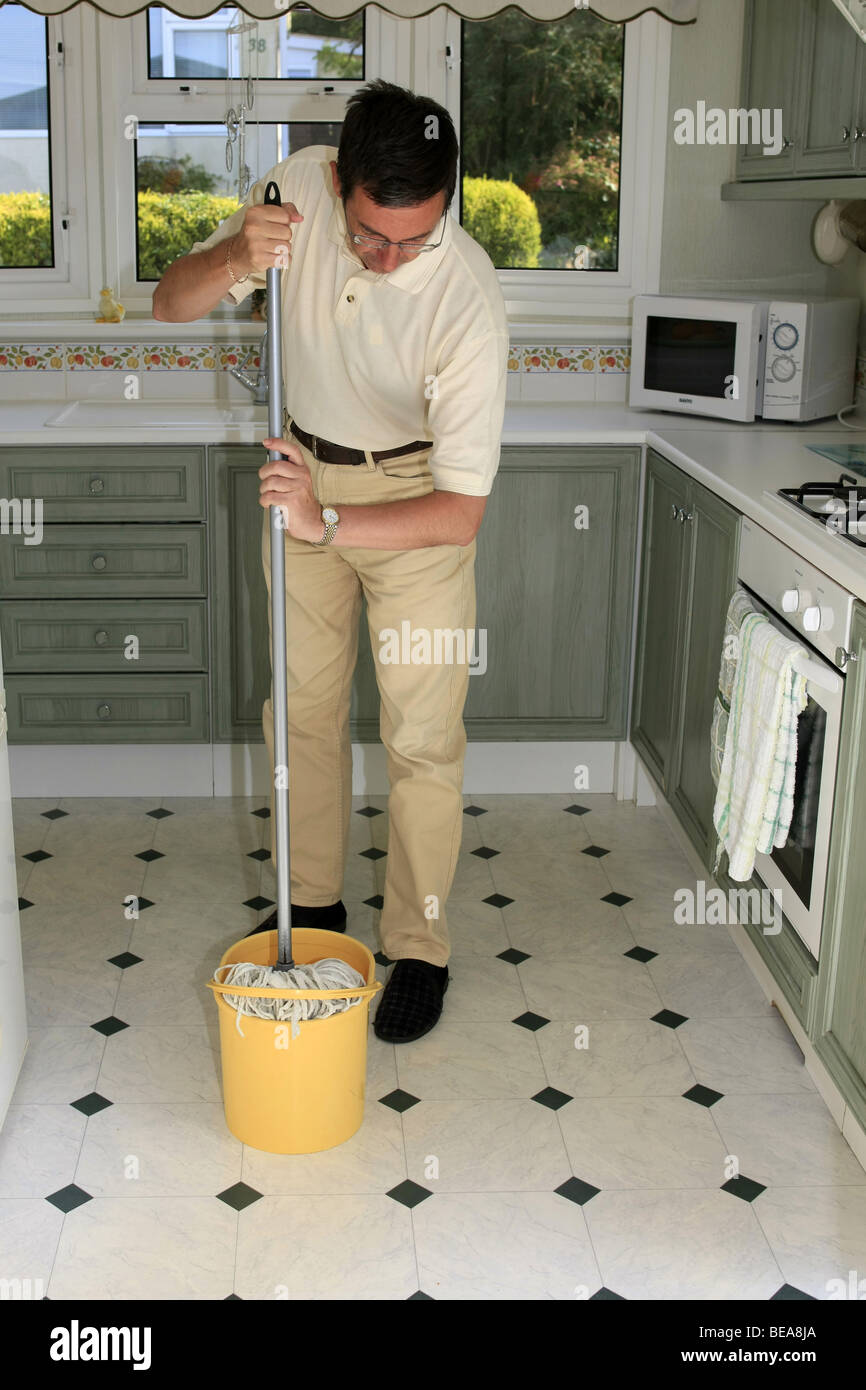 A man using a mop and bucket to clean a kitchen floor Stock Photo