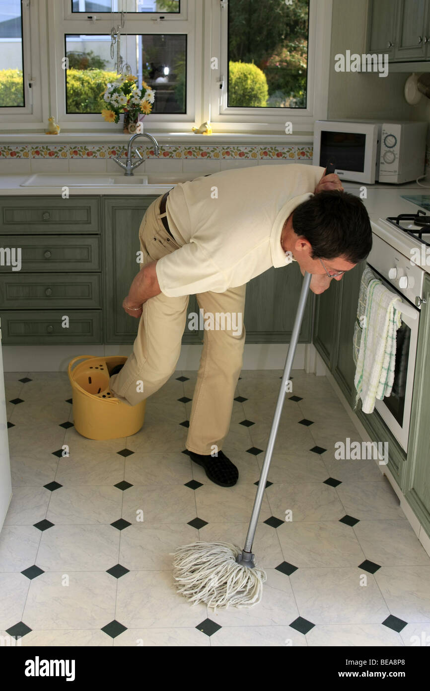A man using a mop and bucket to clean a kitchen floor tripping over the