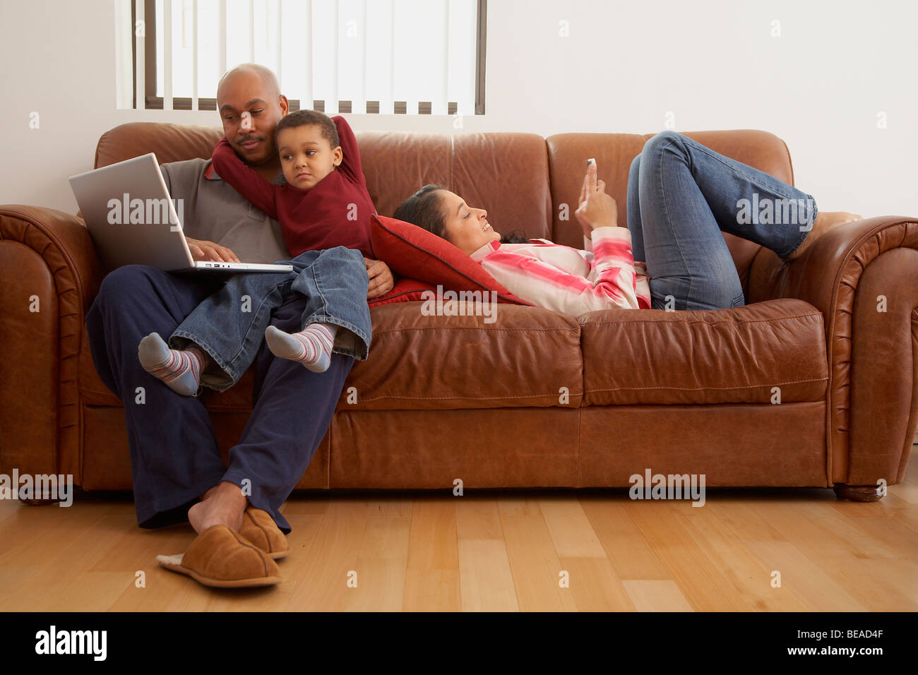Antiguan man using laptop in living room with family Stock Photo