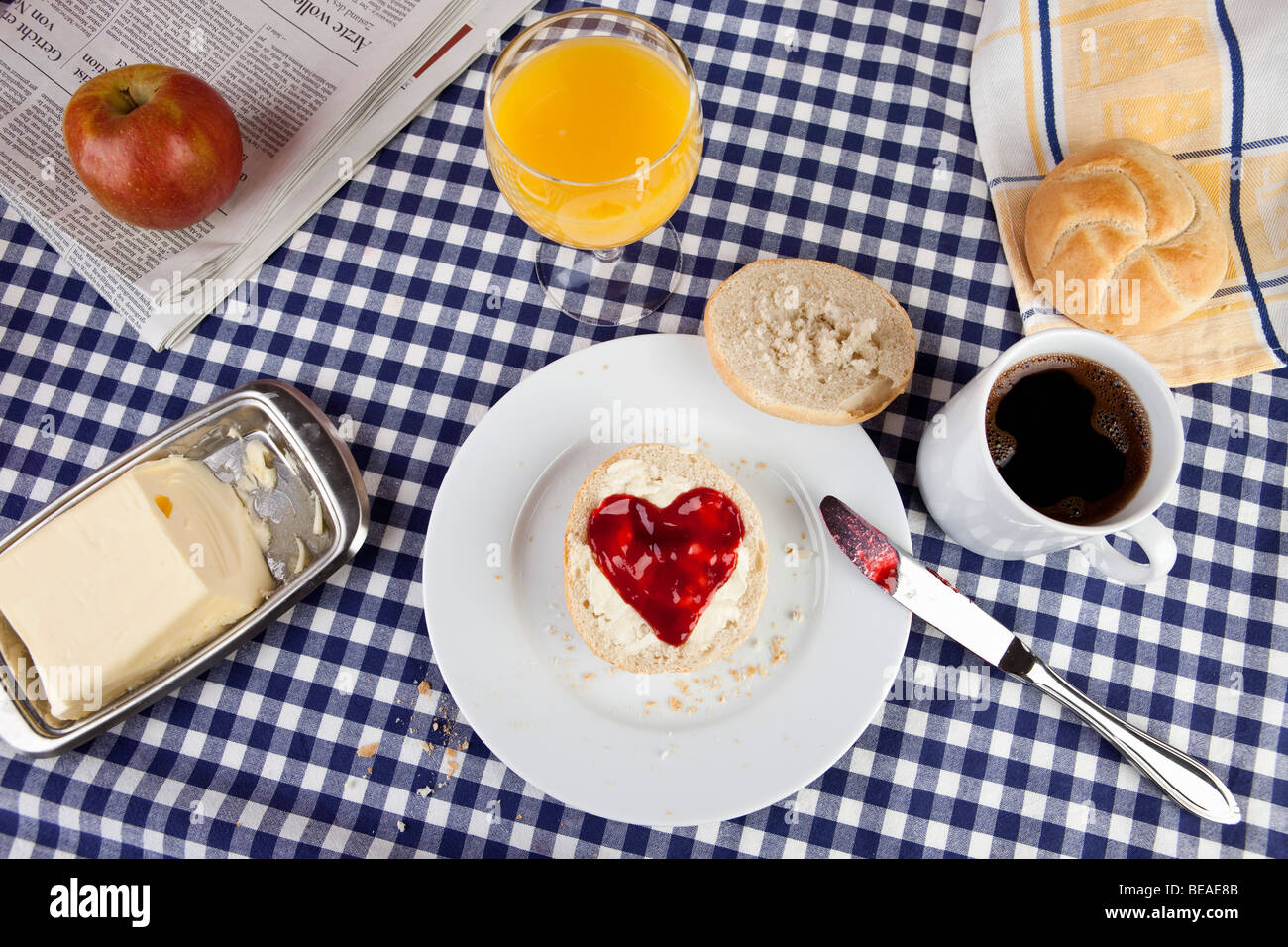 A breakfast table with a bread roll with heart shaped jam on it Stock Photo
