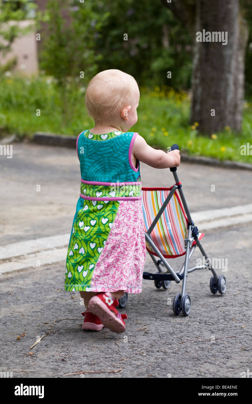 A toddler pushing a baby stroller, rear view Stock Photo