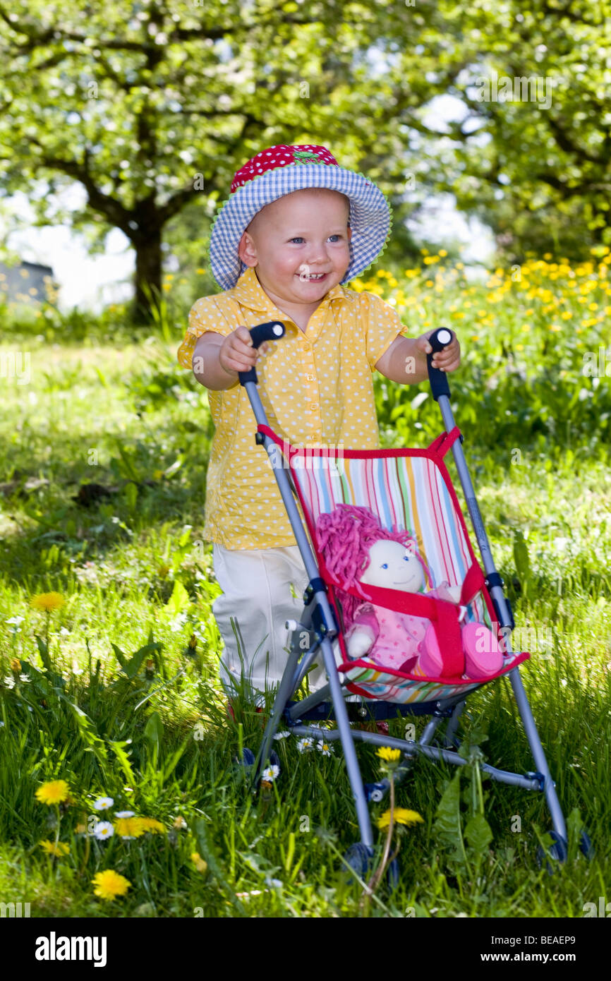 A toddler pushing her doll in a baby stroller Stock Photo