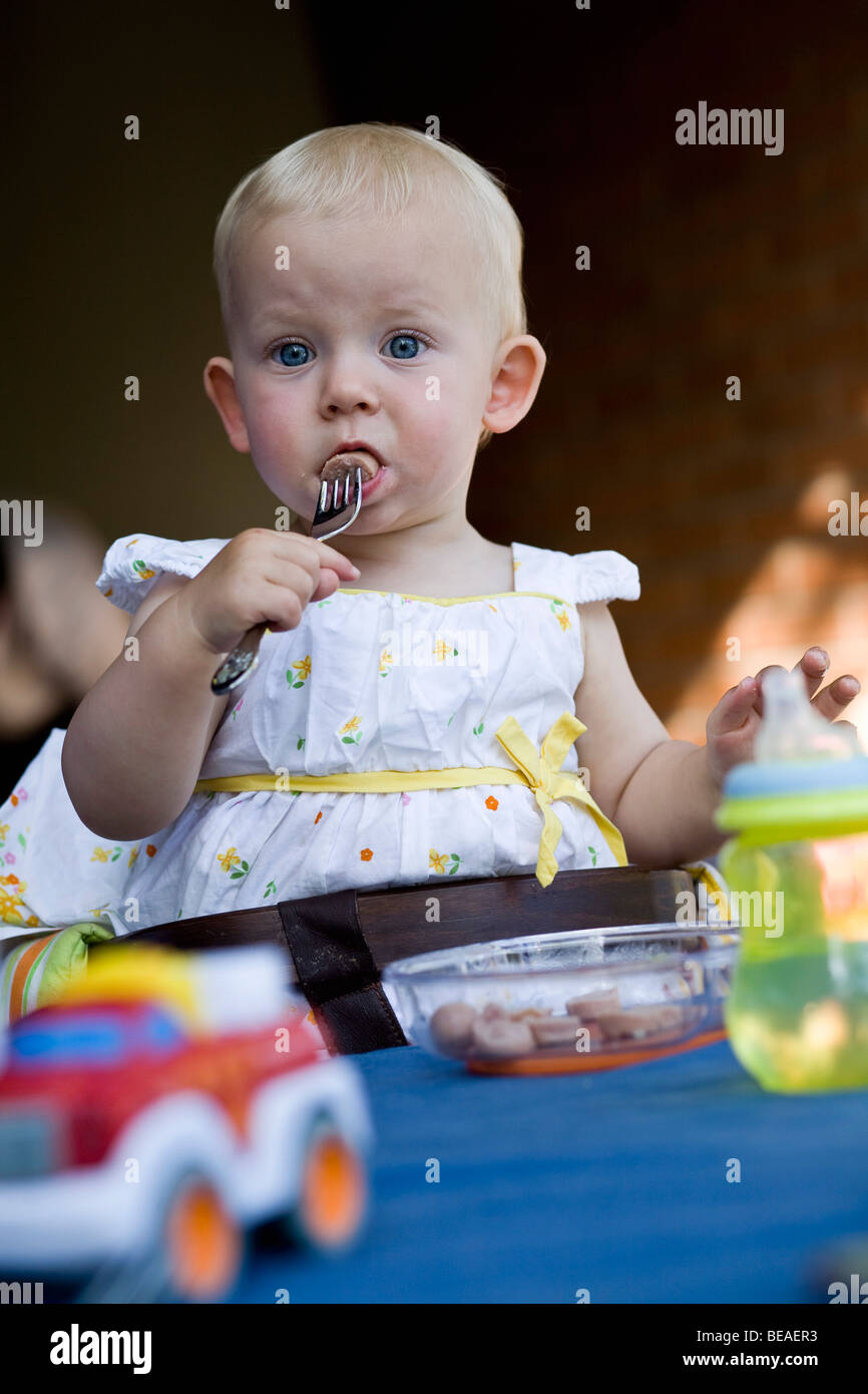 A toddler eating hot dog slices with a fork Stock Photo