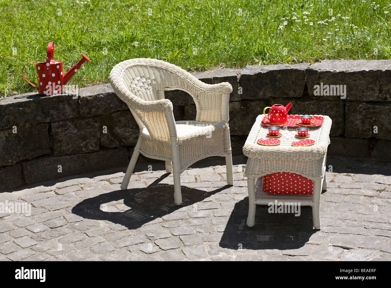A wicker chair and table with a child's tea set, outdoors Stock Photo