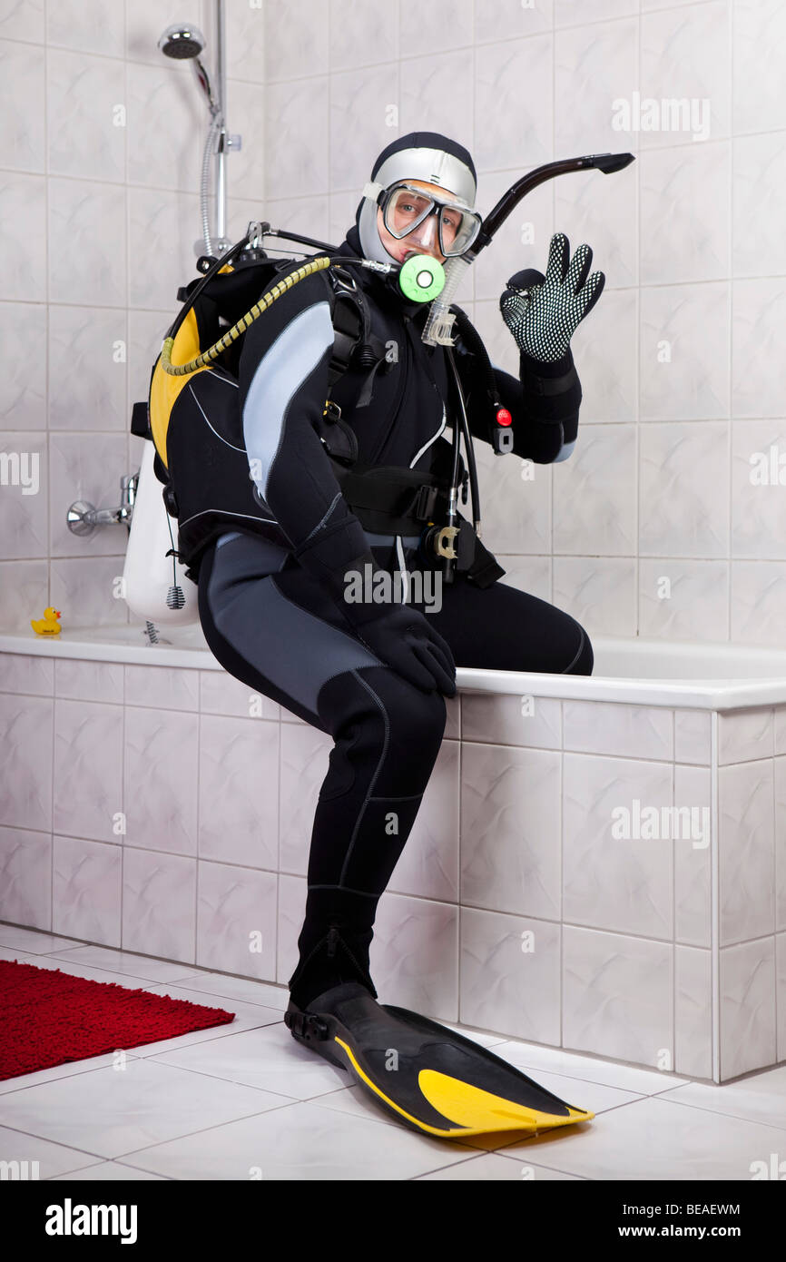 A scuba diver making the OK sign while sitting on the edge of a bathtub