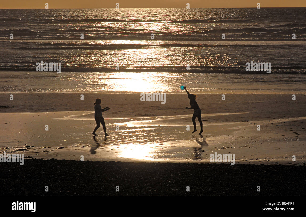 Silhouetted young women playing with a frisbee on beach at Greymouth on South Island, New Zealand. Tasman Sea Stock Photo