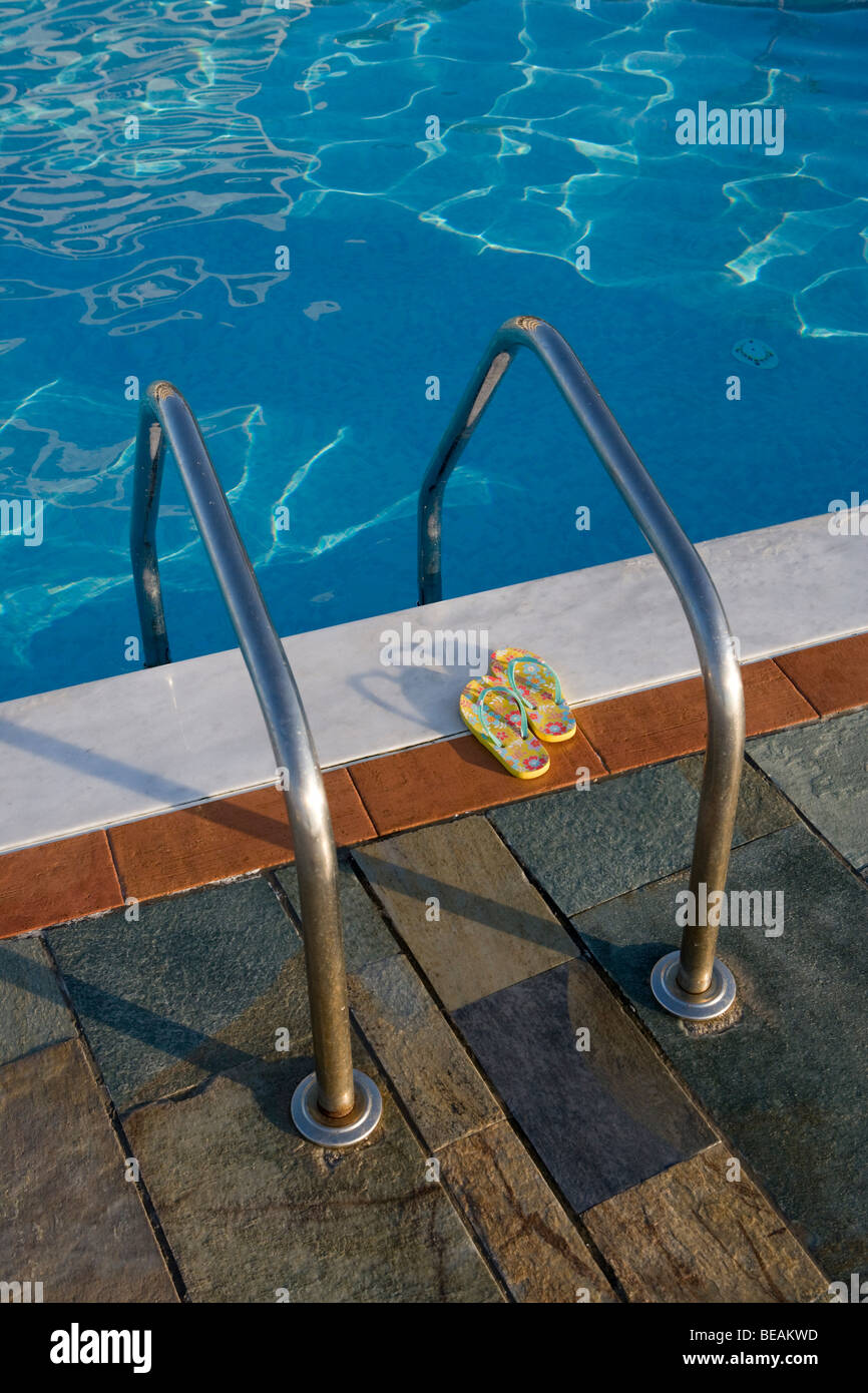 Two flip-flops next to a swimming pool ladder. Stock Photo