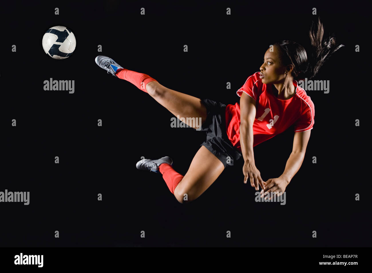 Mixed race soccer player kicking soccer ball in mid-air Stock Photo