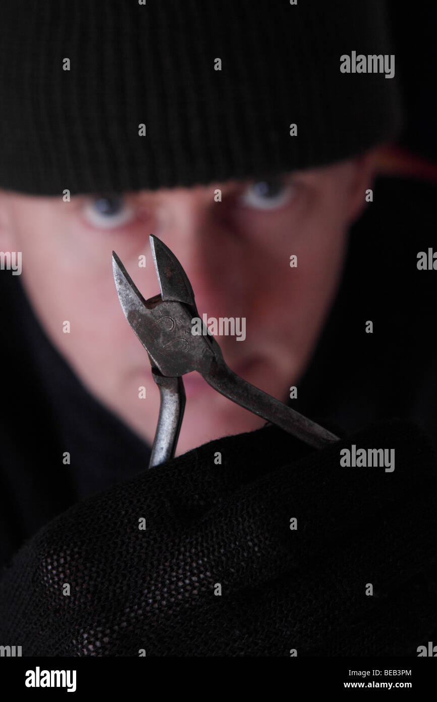 Crime burglar with wire cutters to cut alarm and telephone wire cables and wearing dark black clothing Posed By Model Stock Photo