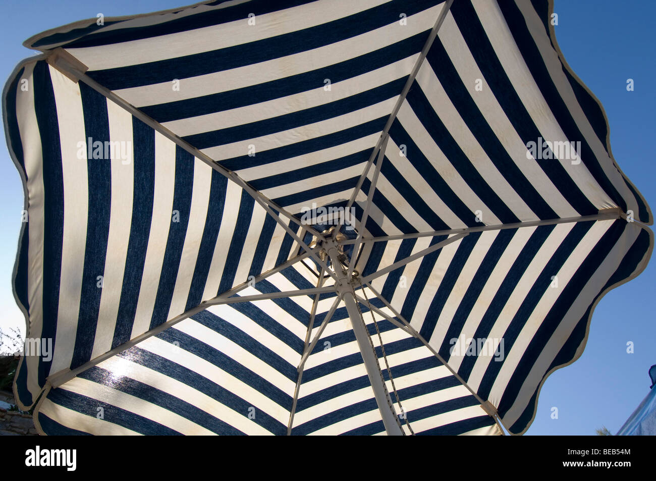 A stripy beach umbrella on a greek island offers shade from the sun Stock Photo