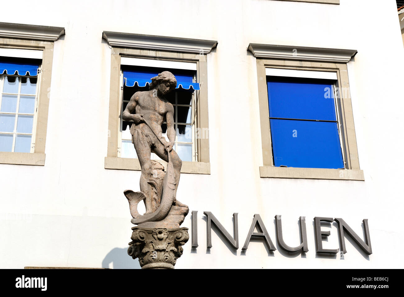Fountain in the Old Town of Zurich, close to Linmat Quay, with a white wall in the background. Stock Photo