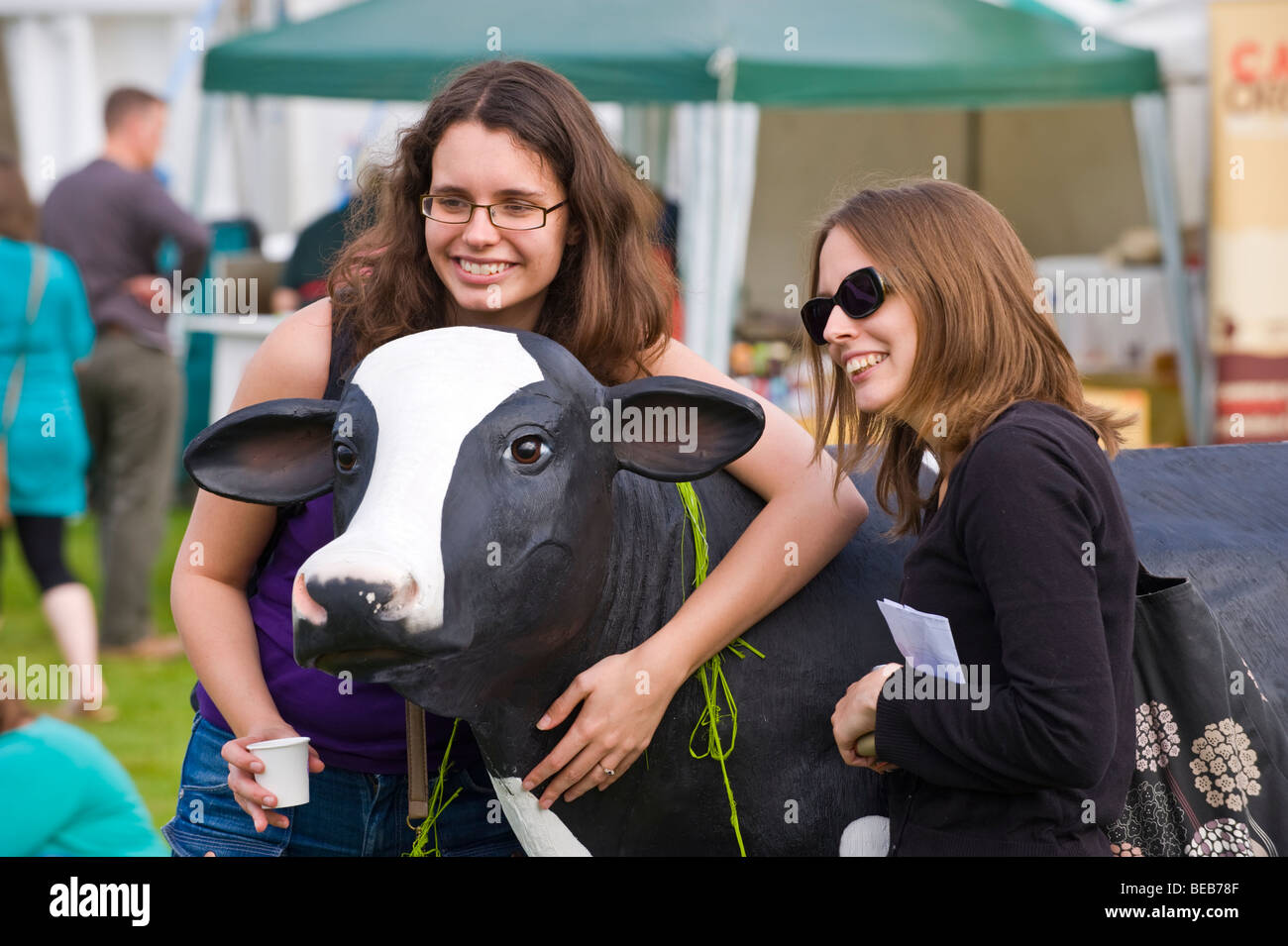 Two young women have their photo taken with promotional plastic cow at The Great British Cheese Festival Cardiff South Wales UK Stock Photo