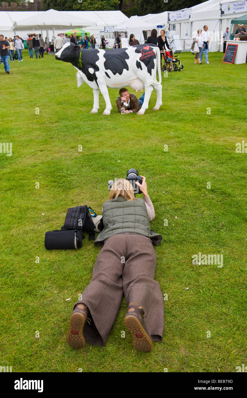 Photographer shooting actor and cheesemaker Sean Wilson under a cow at The Great British Cheese Festival Cardiff South Wales UK Stock Photo