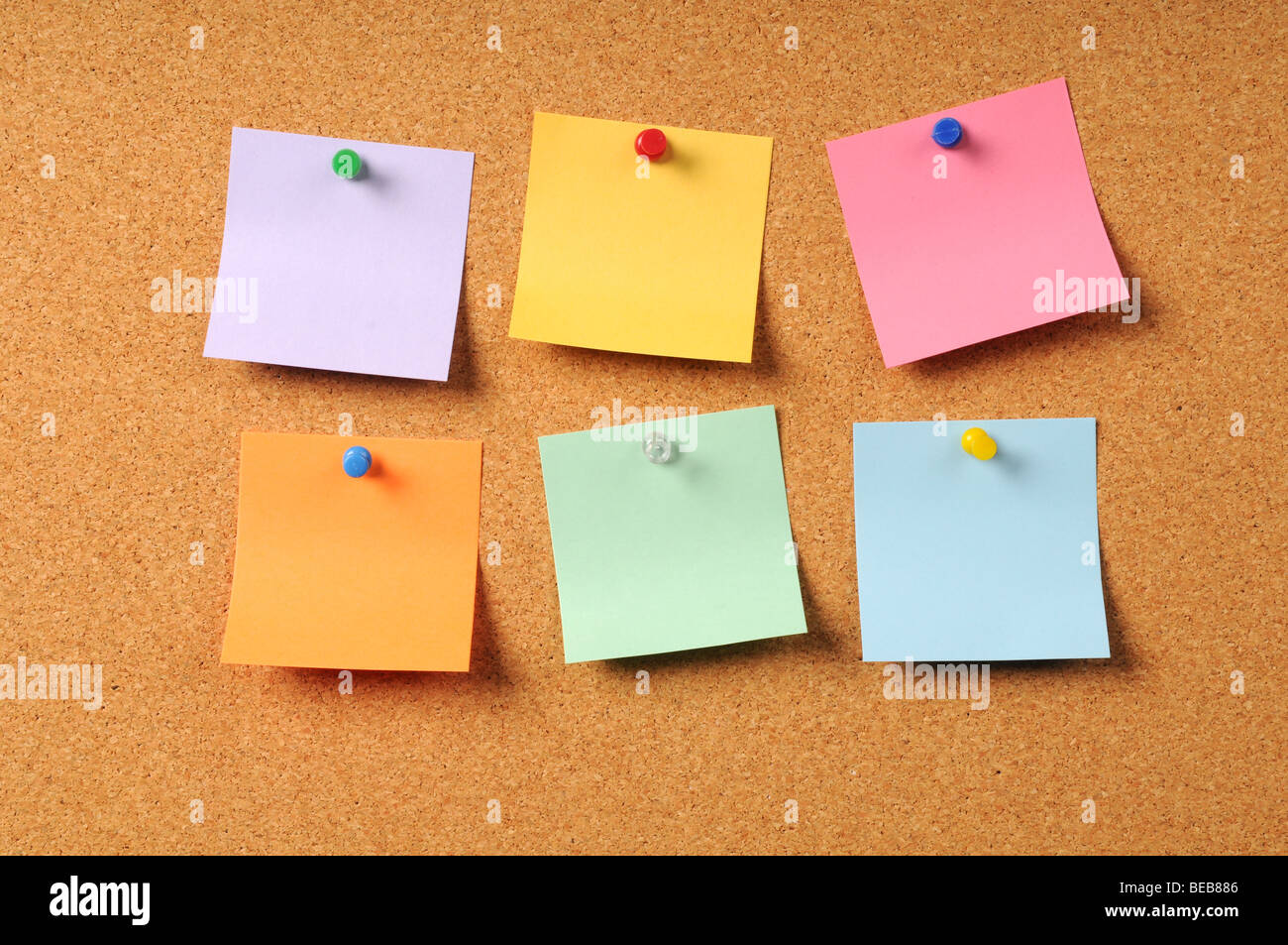 Adhesive notes of various colors pinned to cork surface Stock Photo