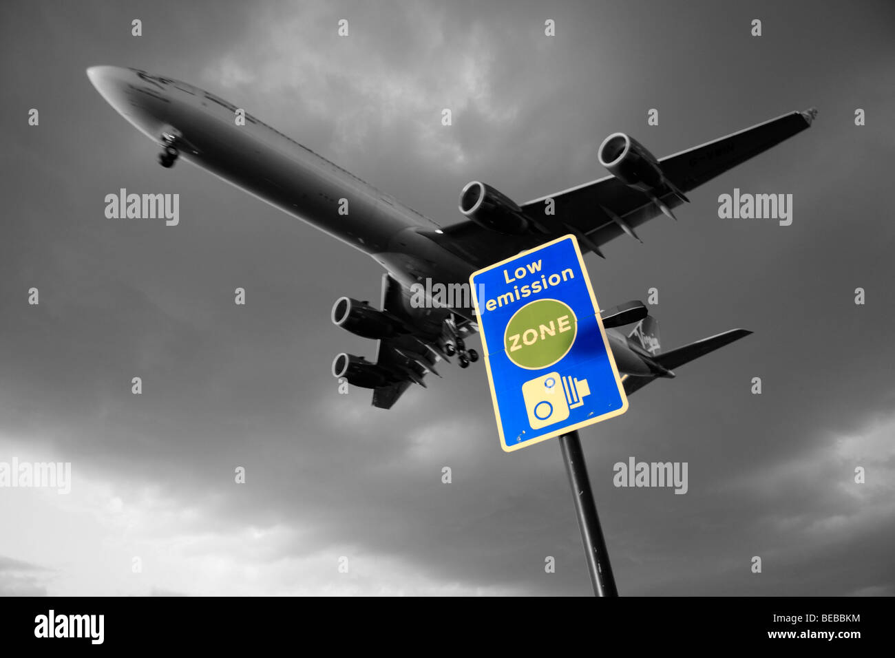 A Virgin Atlantic areplane passes over 'Low Emission Zone' road sign beside London's Heathrow Airport, UK. B&W & Colour mix. Stock Photo