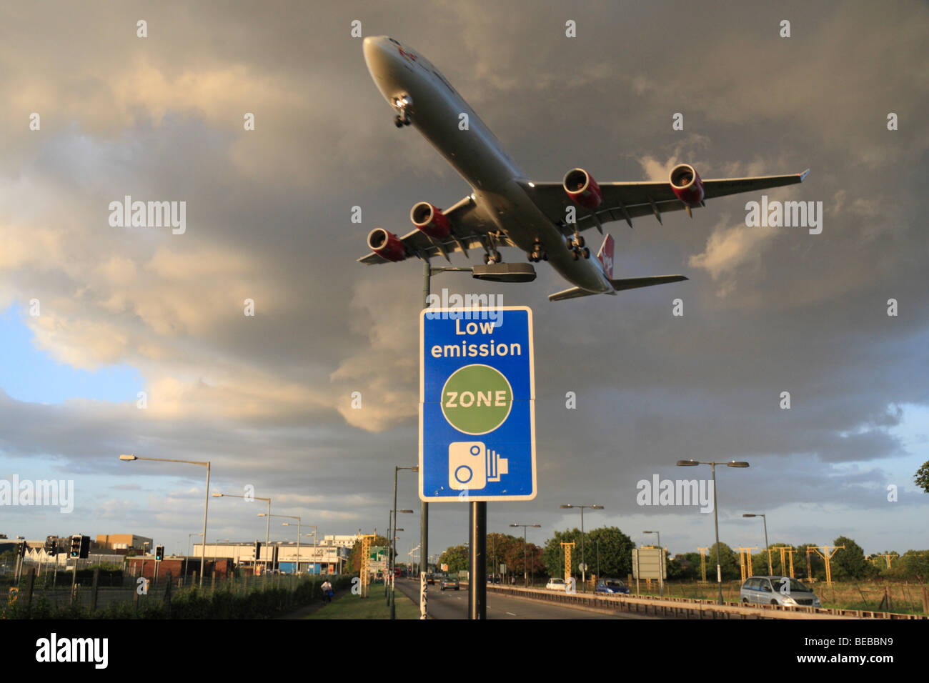 A Virgin Atlantic aircraft passes over a 'Low Emission Zone' road sign beside London's Heathrow Airport, UK. Stock Photo