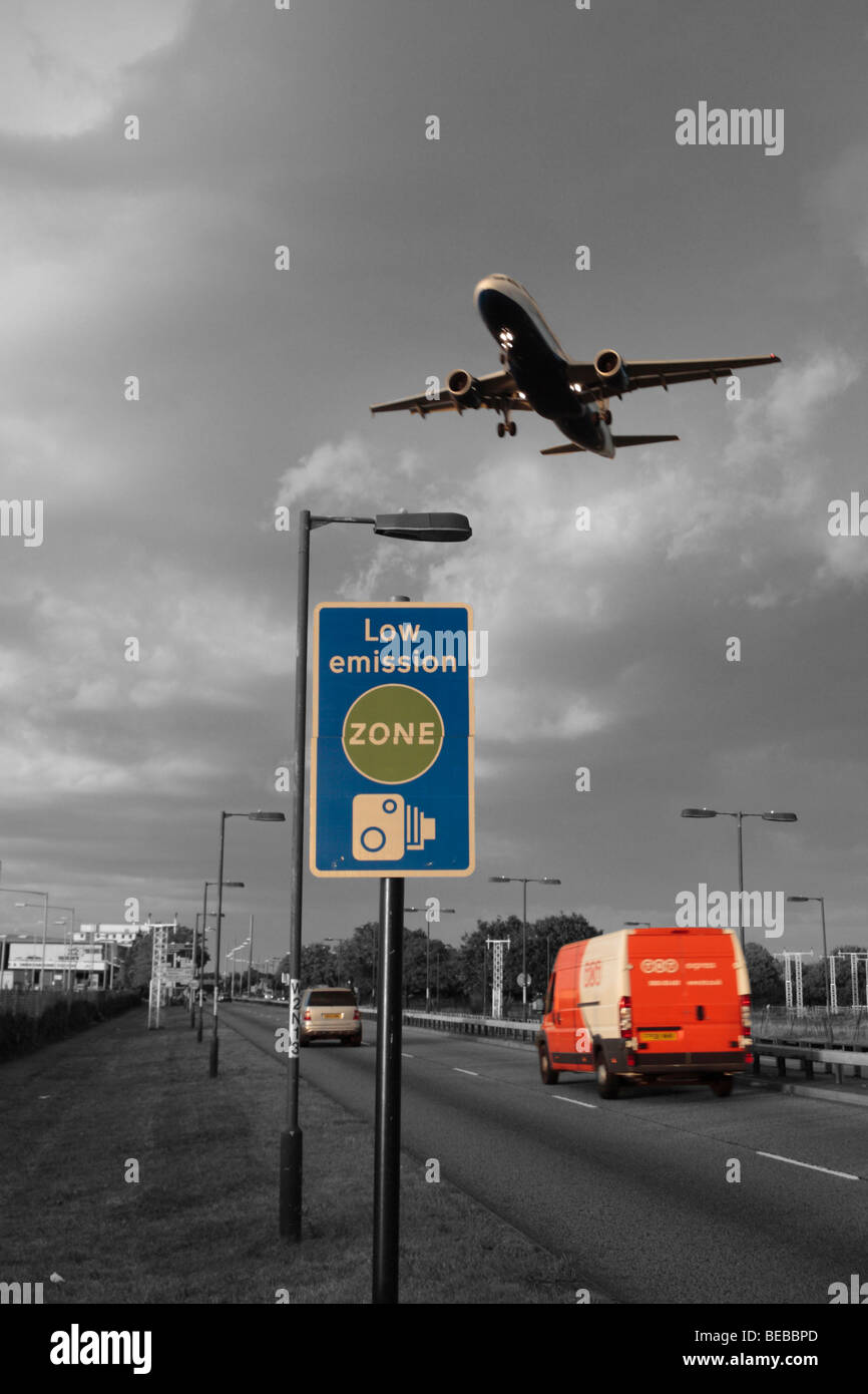 Vans, cars and passing aircraft pass a 'Low Emission Zone' road sign beside London's Heathrow Airport, UK. B&W & Colour mix. Stock Photo