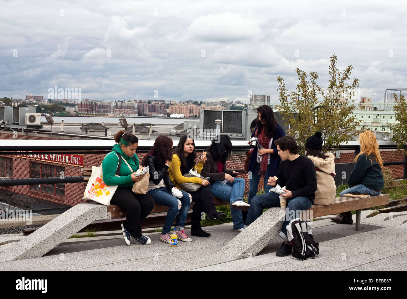 group of teen high school girls & one good-looking boy eat lunch outdoors on benches in an autumnal New York City High Line Park Stock Photo