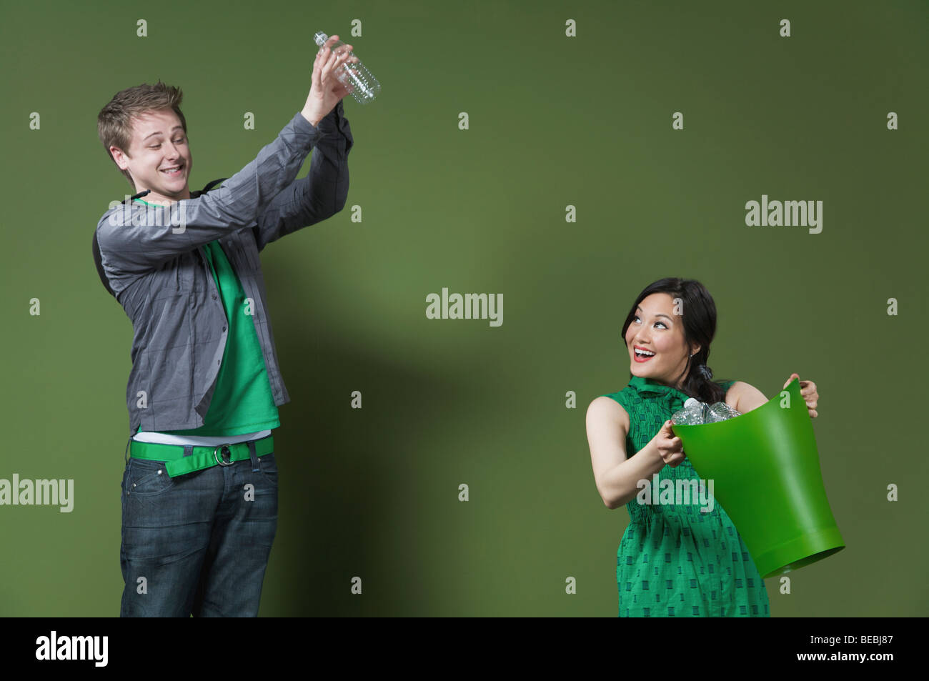 Woman holding a recycling bin and a man throwing an empty water bottle Stock Photo
