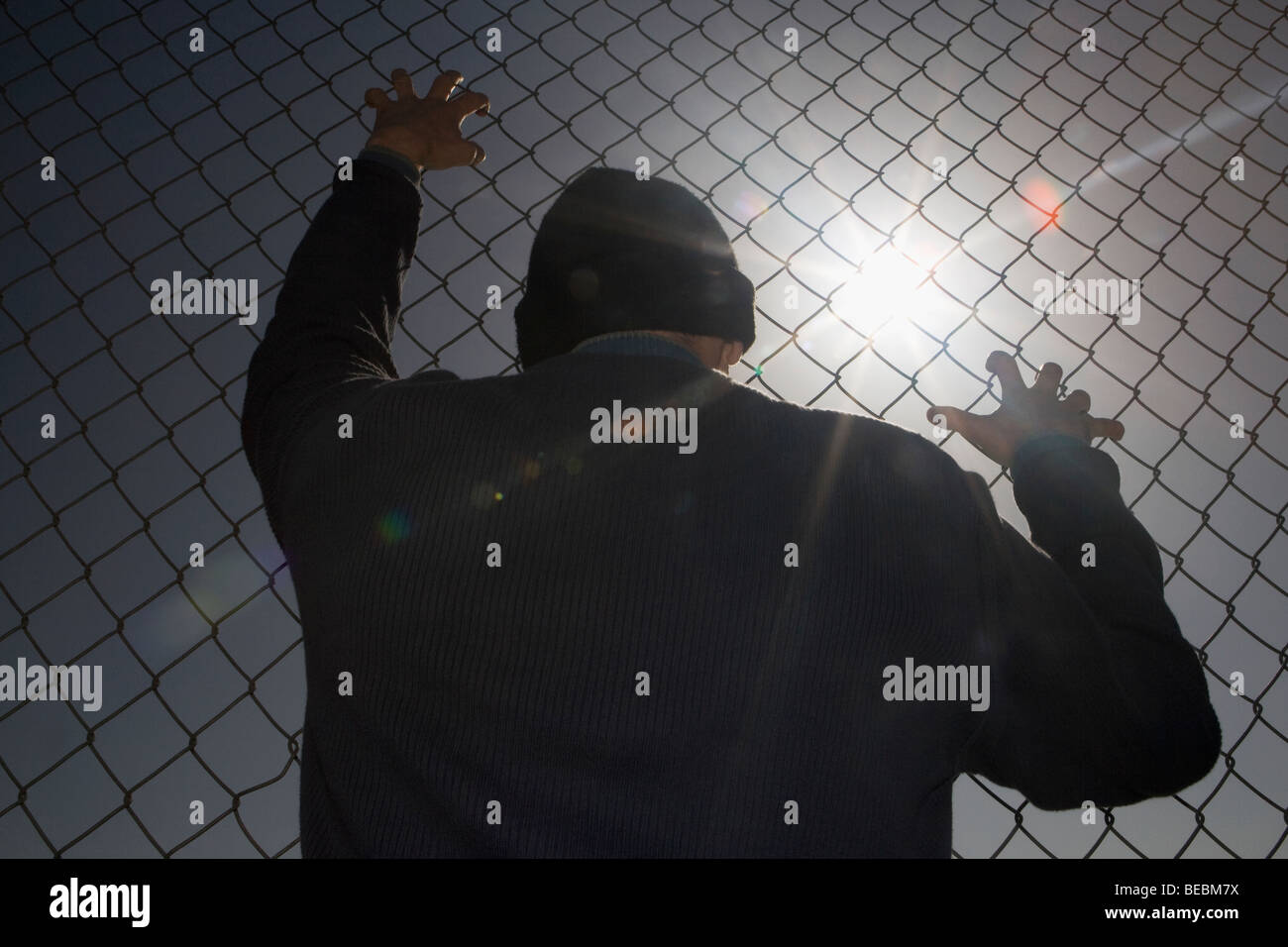 Rear view of a man looking through a chainlink fence Stock Photo