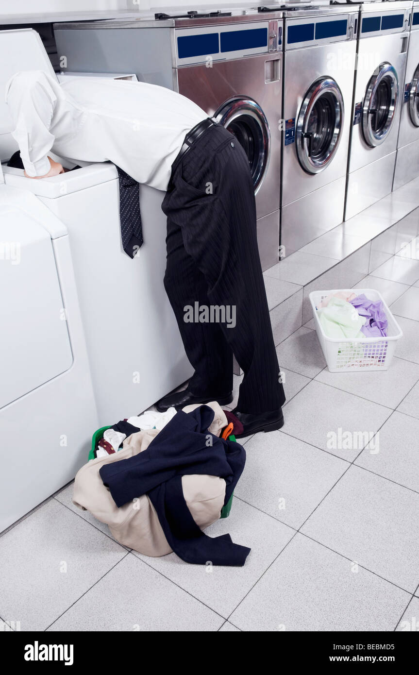 Businessman looking inside the washing machine in a laundromat Stock Photo