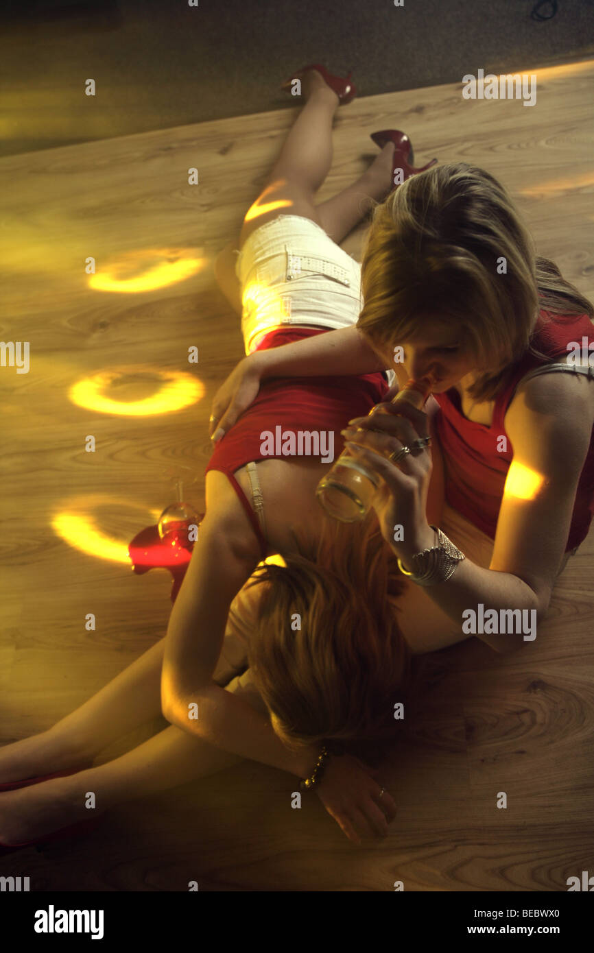 drunk girl lying across the lap of a girl sitting on a dance floor Stock Photo