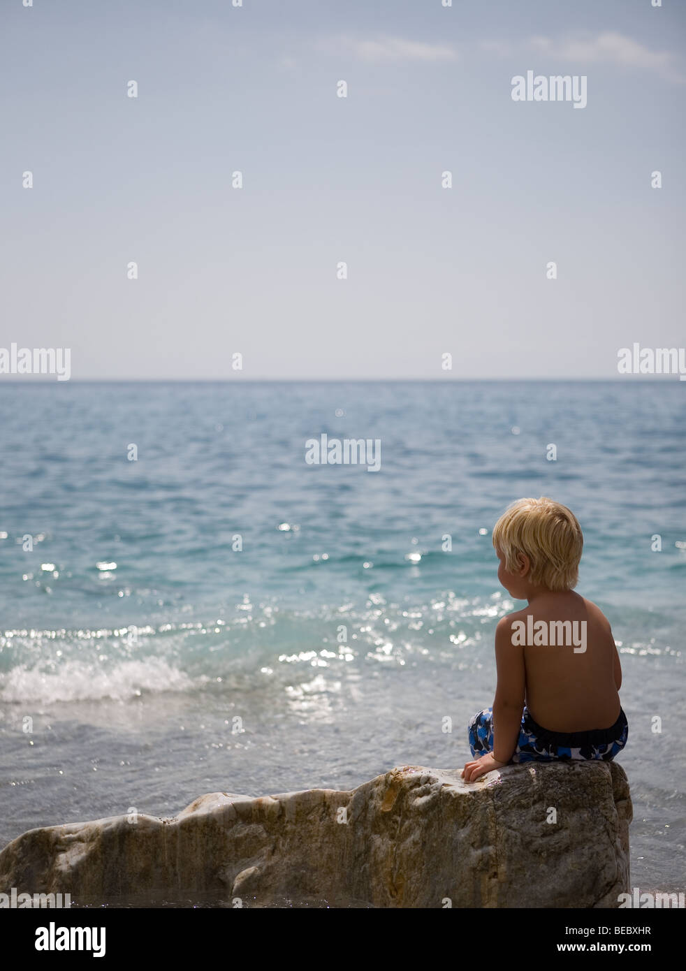 little kid watching the beautiful sea while sitting on a rock Stock Photo