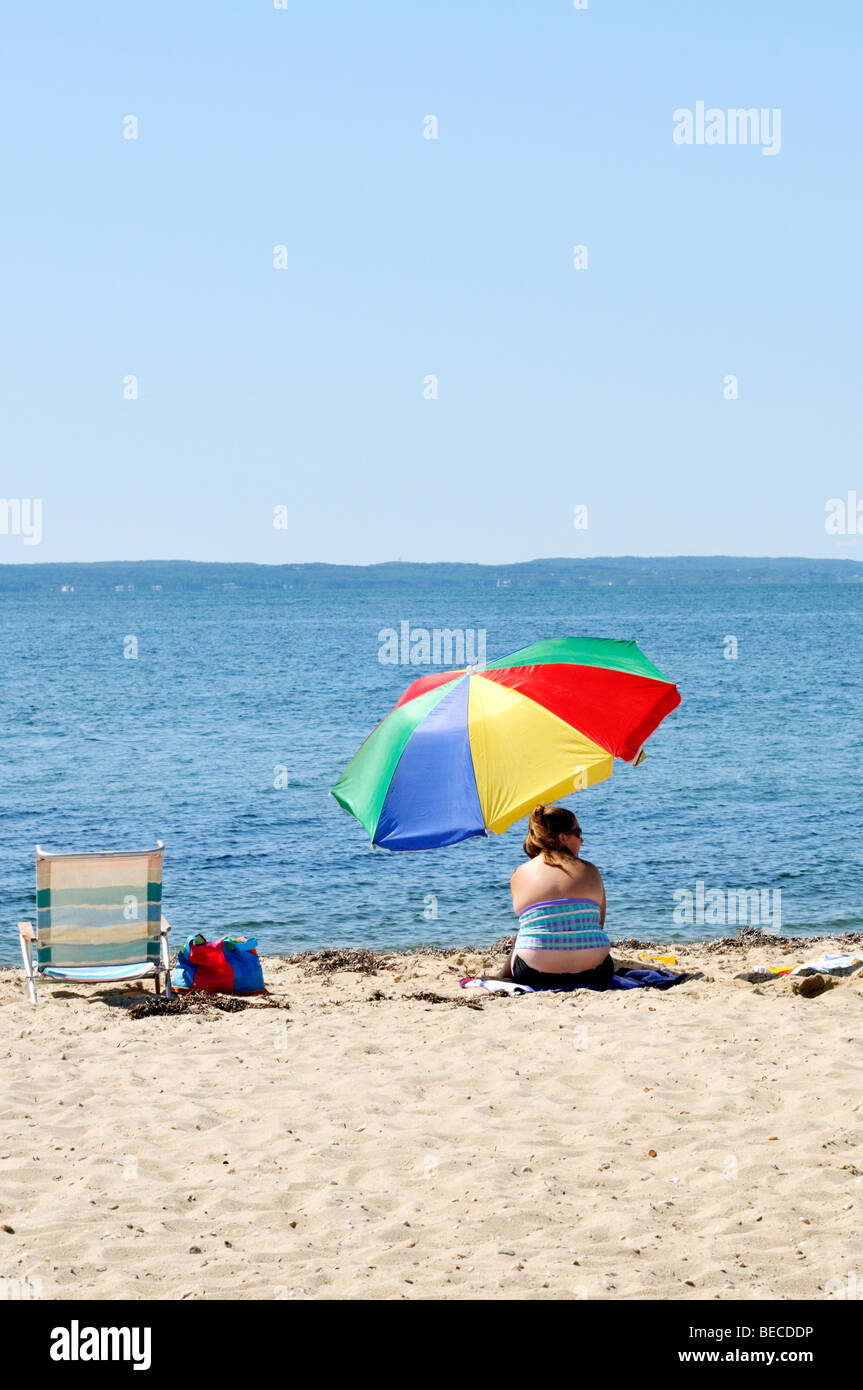 Woman on Cape Cod beach under colorful umbrella on a sunny summer day. Stock Photo