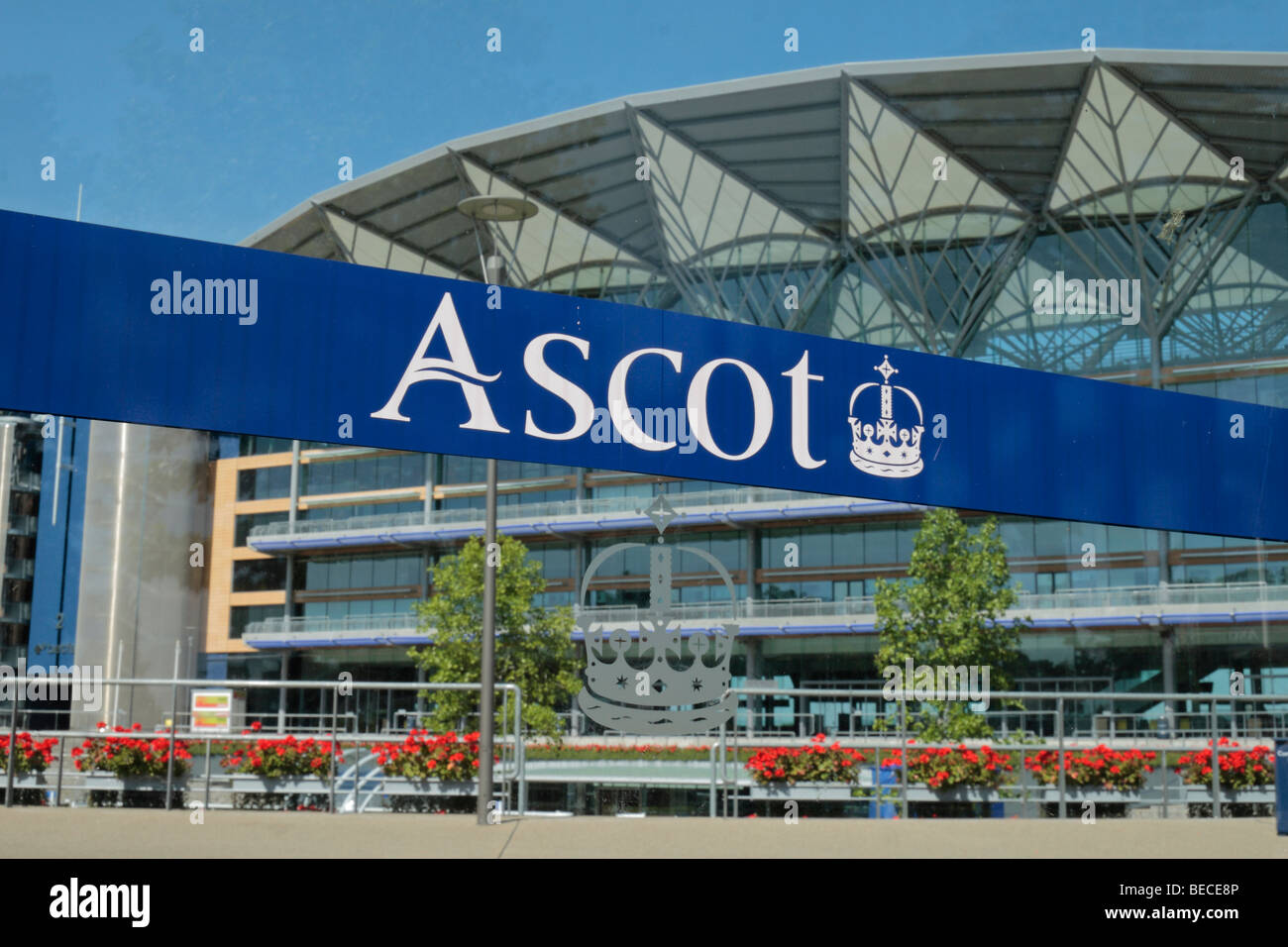 View through a glass panel with the 'Ascot' name and logo towards the main Grandstand at Ascot Racecourse, Berkshire, UK. Stock Photo