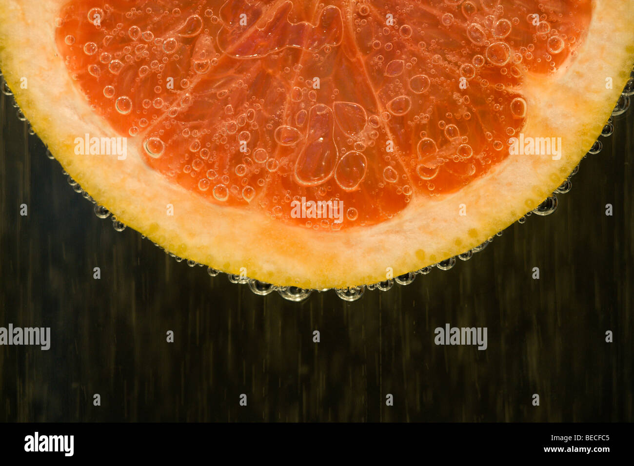 Close-up image of a section of a red / ruby grapefruit slice surrounded by bubbles of water Stock Photo