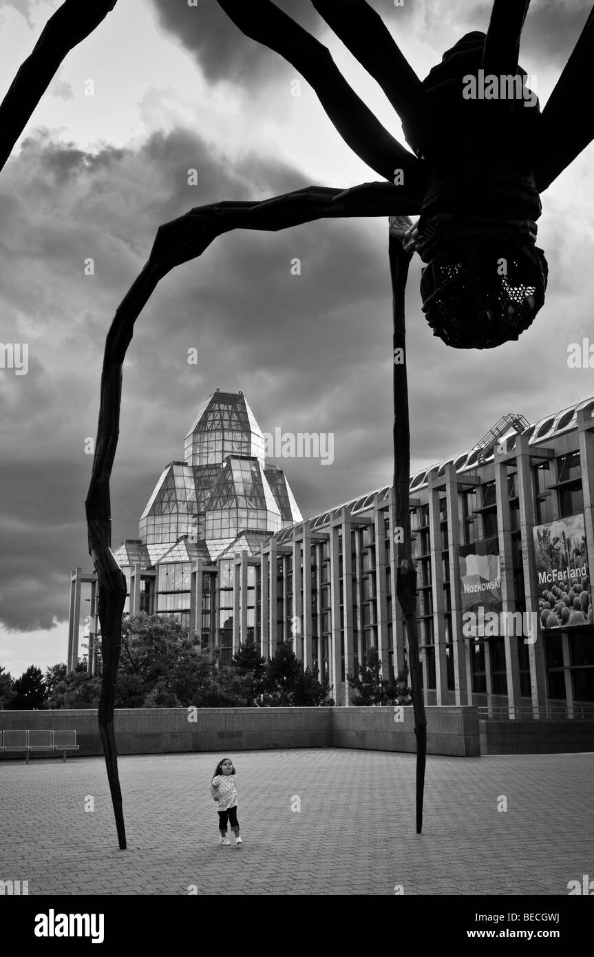 A yong girl stops to stare up at 'Maman'; a giant spider sculpture created by Louise Bourgeois dwarfs the National Art Gallery. Stock Photo