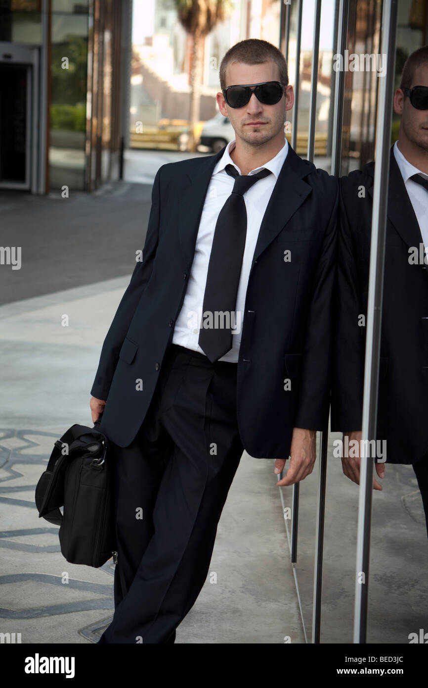 businessman leaning against a modern glass building Stock Photo