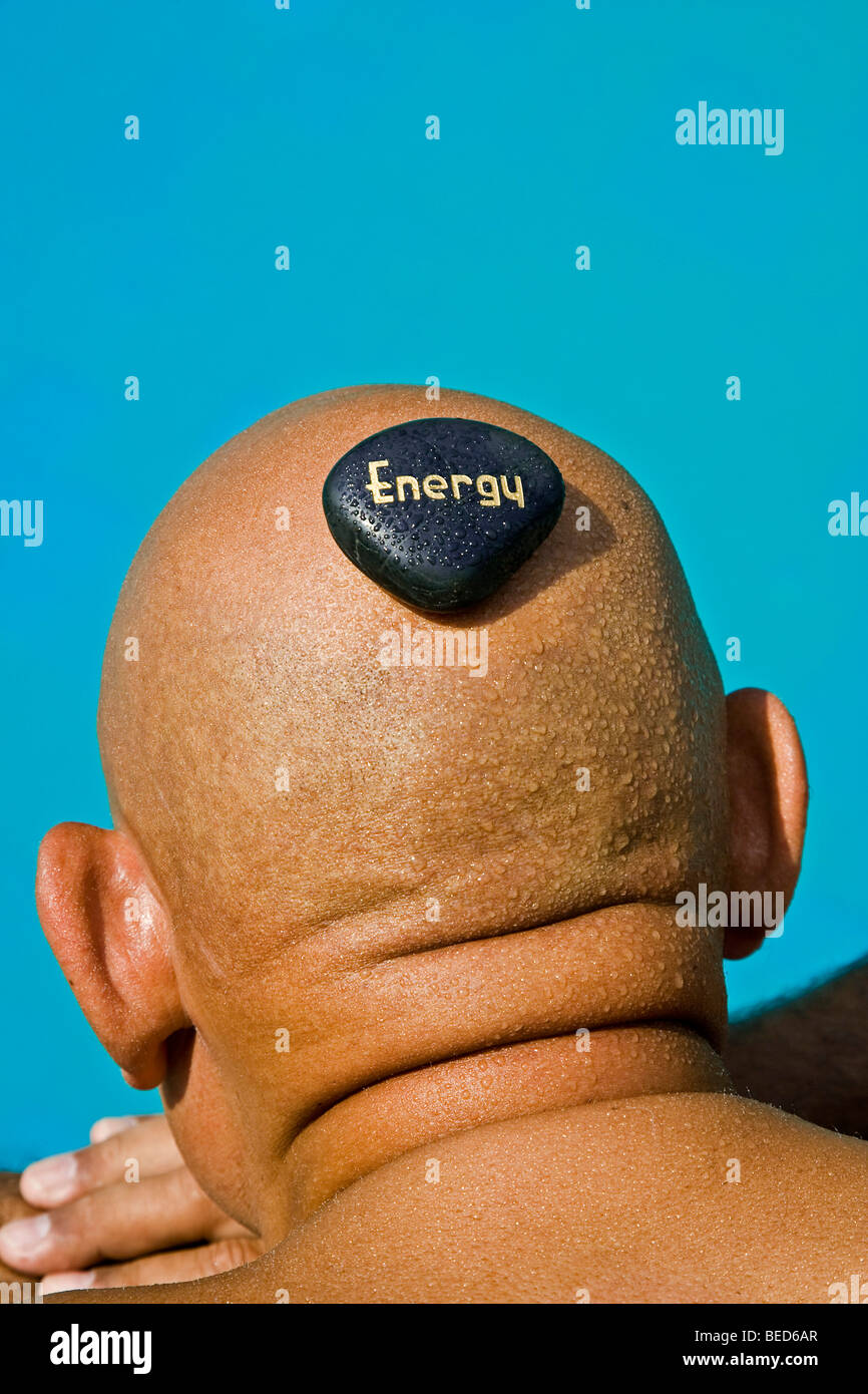 A stone with the writing 'Energy' lying on the bald head of a man Stock Photo