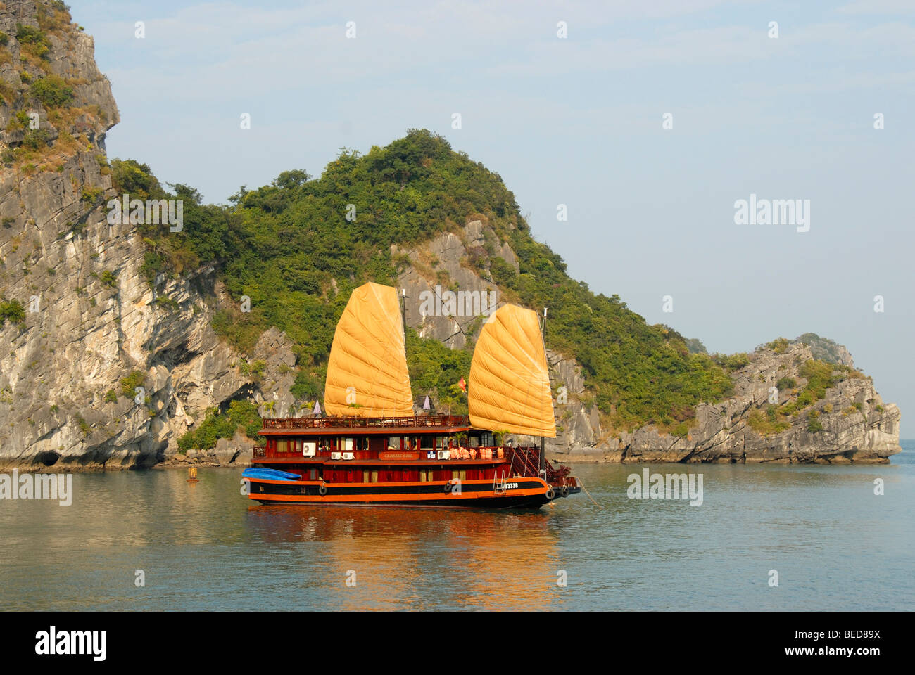 Typical sailing ship, Junk, with two yellow sails in front of a rocky island, Ha Long Bay, Vietnam, Asia Stock Photo