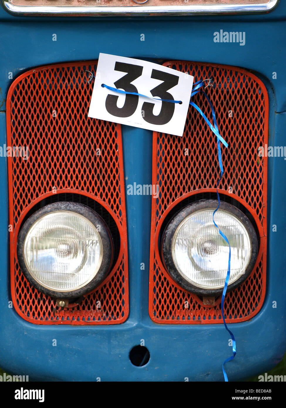 shiny silver headlamps peep through red grill on blue tractor - entry no. 33 at vintage tractor show Stock Photo