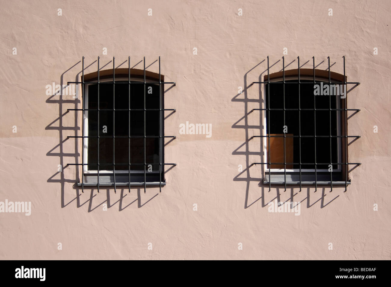 A pair of windows with grilles and shadows on a house front Stock Photo